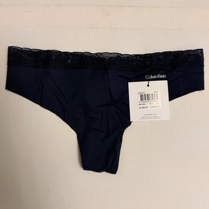 A pair of Calvin Klein navy blue lace-trimmed panties with a white retail tag attached, laid flat against a light off-white textured background.