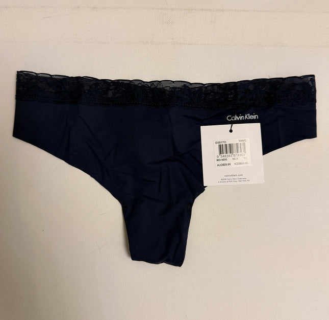 A pair of Calvin Klein navy blue lace-trimmed panties with a white retail tag attached, laid flat against a light off-white textured background.