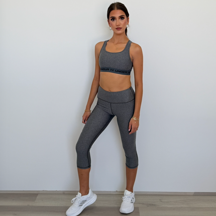 Woman wearing a gray athletic outfit standing against a white wall.